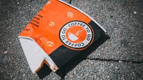 Ein Einwegbecher für Kaffee liegt auf dem Boden. Die Plastikbeschichtung aus Polyethylen zersetzt sich mit der Zeit zu kleinen Plastikpartikeln - Mikroplastik. Dieses ist eine Belastung für Böden, Gewässer und Tiere.
