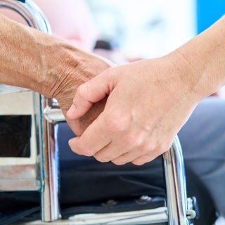 Nahaufnahme eines Pflegepersonals, das die Hand eines älteren Patienten in einem Rollstuhl hält, der Unterstützung und Hilfe während der Rehabilitation bietet. | Pflege auf dem Land: Wie Gemeindeschwestern Senioren helfen