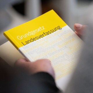 Ein Mann hält das Grundgesetz und eine Landesverfassung in den Händen