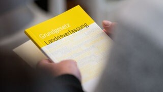 Ein Mann hält das Grundgesetz und eine Landesverfassung in den Händen