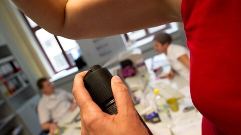 Eine Frau sprüht sich ein Deodorant in einem Büro unter die Achseln. (Symbolbild)