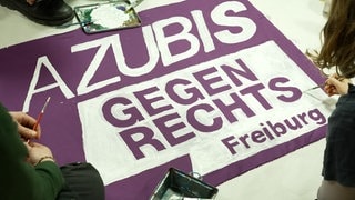 Auf einem lila Banner steht mit weißer Farbe geschrieben: Azubis gegen Rechts.