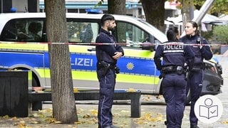 Ein Polizeiauto und drei Polizisten stehen vor dem Rathaus in Tuttlingen. Davor ist ein Absperrband von der Polizei. Die Polizei hat einen Mann erschossen. Rechts das SWR Logo für Leichte Sprache.