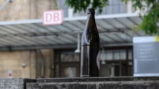 Eine Bierflasche steht vor einem Bahnhof auf einer Bank. Die Deutsche Bahn plant einen radikalen Schritt mit der Hoffnung auf mehr Sicherheit für die Fahrgäste und die Beschäftigten.