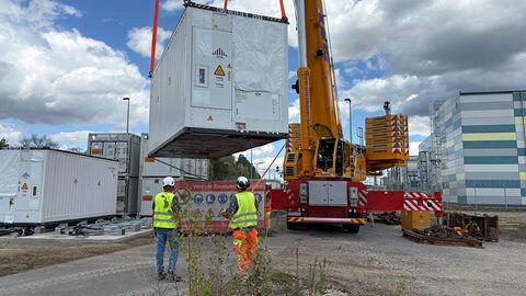 Der Kran hebt einen Batterie-Container auf das Fundament.