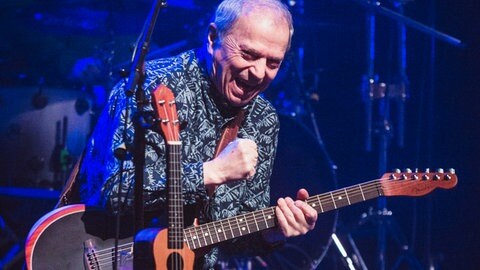 Günther Sigl steht mit der Gitarre in der Hand auf der Bühne und singt ins Mikrofon
