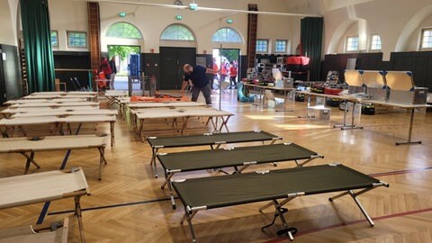 Mehrere aufgebaute Feldbetten in einer Halle als Notunterkunft nach einem Stromausfall.
