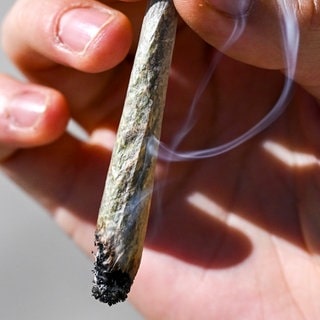Ein qualmender Joint in einer Hand. Nicht alles, was in einem Hanfladen in der Innenstadt verkauft wurde, war laut Stadt Heidenheim legal (Symbolbild).