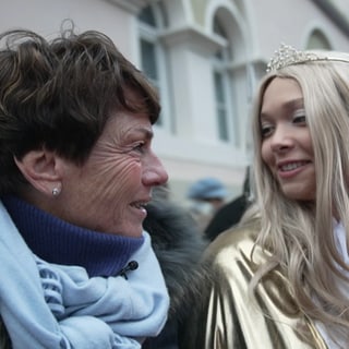 Sonja Faber-Schrecklein lächelt eine junge Frau an, die als Christkind verkleidet ist und eine Krone und einen goldenen Umhang trägt.