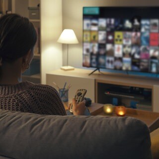 Frau sitzt am Abend auf dem Sofa vor dem Fernseher