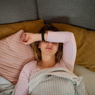 Eine Frau liegt auf einem Sofa und leidet unter Kopfschmerzen.