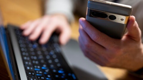 Ein Mann sitzt mit Smartphone am Laptop. 