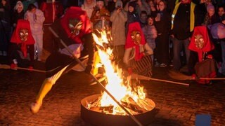 Maskierte Hutschelhexen springen um ein Feuer. In Bad Bergzabern wird der Start der Fastnacht mit Guggemusik, Totenköpfen und Feuer gefeiert.