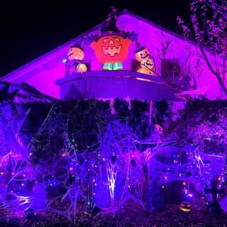 Ein Haus ist mit Halloween-Dekorationen geschmückt. Spinnweben, Grabsteine, Kürbisse und Lichteffekte sind zu sehen.
