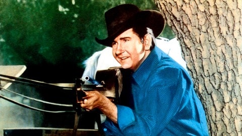 Sänger Roy Orbison als Schauspieler in dem Film "The Fastest Guitar Alive" trägt einen Hut und hält eine Gitarre wie ein Gewehr.