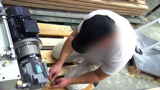 Insasse der JVA Mannheim arbeitet im Malerbetrieb. Er kniet auf einer Palette und arbeitet an einer Maschine.