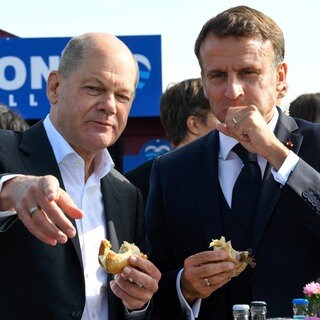 Bundeskanzler Olaf Scholz (SPD) und Frankreichs Präsident Emmanuel Macron (rechts) essen im Oktober 2023 in Blankenese ein Fischbrötchen. Gemeinsames Speisen ist eines der ältesten Instrumente der Diplomatie, um Verständigung und Kooperation zu fördern.