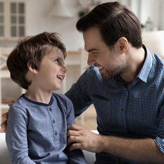 Vater mit kleinem Sohn im vertraulichen Gespräch: Sexualaufklärung ist wichtig. Altersgerechte Begriffe wie Penis oder Vulva helfen, Scham zu vermeiden und stärken den Schutz vor Missbrauch, weil Kinder Dinge klar benennen können.
