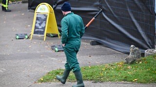 Ein Arbeiter in Schutzkleidung läuft an einer Absperrung eines Geflügelbetriebes in Öllingen. Die Familie des Betriebs ist schockiert.