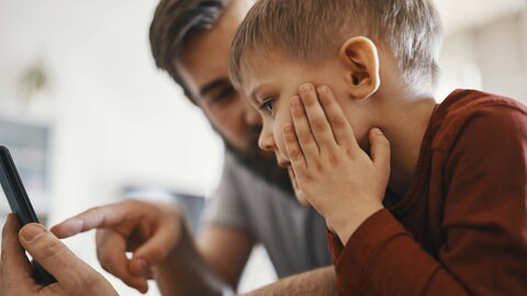 Vater und Sohn schauen auf ein Handy.