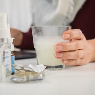 Eine Person nimmt Aspirin, daneben Taschentücher und Nasenspray. In Deutschland ist aktuell jeder Elfte krank.