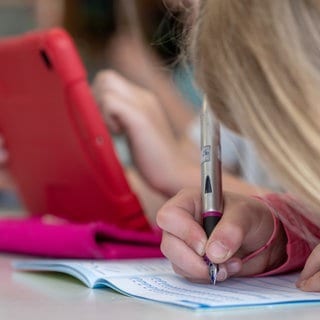 Ein Mädchen schreibt mit einem Füller in ein Schulheft: Das neue Schuljahr hat in RLP begonnen, eine Neuerung ist: Es gibt keine unangkündigten Überprüfungen der Hausaufgaben mehr. (Symbolbild: Schülerin schreibt in ihr Heft)