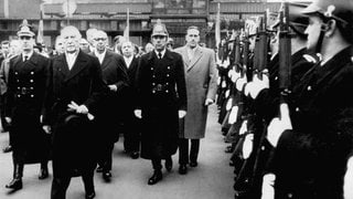 Bundeskanzler Konrad Adenauer (2.v.l.) schreitet am 1. Januar 1957 die Polizeihundertschaft ab, hinter ihm der Ministerpräsident der Saarregierung, Hubert Ney