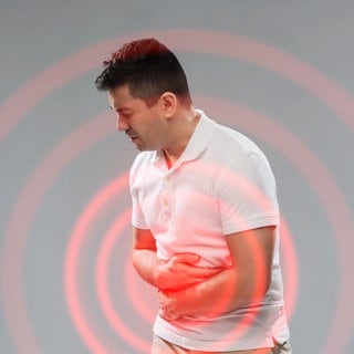 Ein junger Mann hält sich mit beiden Armen den Bauch. Es scheint, er hat Probleme in der Bauchregion. Heftige Bauchschmerzen und Durchfall können Symptome für chronisch-entzündliche Darmerkrankungen sein. Es gibt diverse Therapiemöglichkeiten.