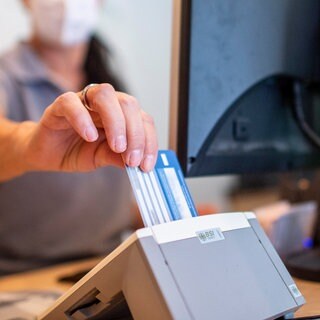 Eine Person schiebt eine Versichertenkarte einer Krankenkasse in eine Lesegerät. Elektronische Rezepte und digitale Patientenakten sollen nach jahrelangen Verzögerungen auf breiter Front zum Einsatz kommen.