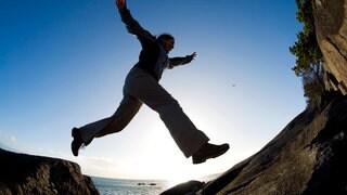 Eine Frau springt beim Wandern auf einen nahegelegenen Fels