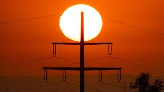 Ein Strommast vor einer aufgehenden Sonne in einer Hitzewelle im Sommer.