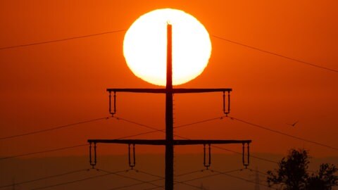 Ein Strommast vor einer aufgehenden Sonne in einer Hitzewelle im Sommer.