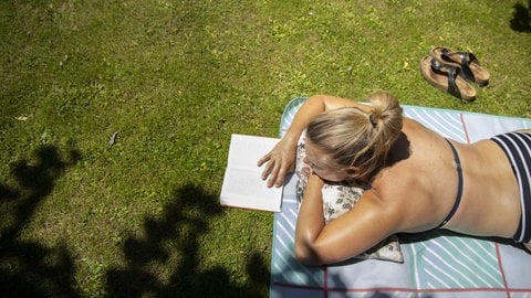 Eine junge Frau liegt auf einer Picknickdecke und liest ein Buch.