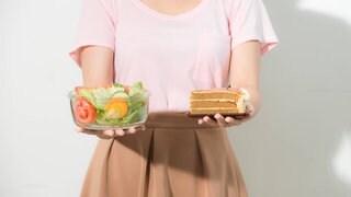 Frau hält in einer Hand eine Schale Salat, in der anderen ein Stück Torte: Eine Ernährungsumstellung ist ein langer Prozess. Man braucht für eine Veränderung des eigenen Essverhaltens Antrieb von außen, z.B. vom Hausarzt oder der Familie. Die kann motivieren und unterstützen: "Das hast du gut gemacht" oder "Komm, probier's noch mal". 