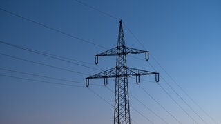 (Symbolbild) Ein Strommast ist bei Sonnenaufgang als Silhouette zu sehen. In Baden-Baden ist der Strom ausgefallen.