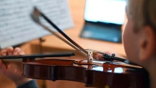 Ein Mann spielt Geige vor seinem Laptop. Die Bodensee-Ouvertüre ist das erste Werk der Bodensee Philharmonie, das von einer KI komponiert worden ist. (Symbolbild)