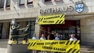 Politikerinnen und Politiker aus Bad Kreuznach protestieren gegen leere Kassen. Sie haben am Eingang des Rathauses symbolisch Absperrband aufgehängt 