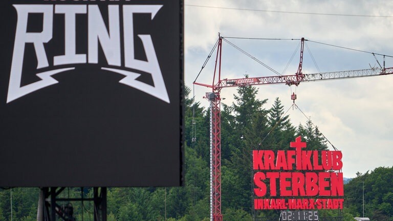 Ein großes, auffälliges Schild leuchtet an einem Baukran mit roter Schrift: „KRAFTKLUB STERBEN IN KARL-MARX-STADT“.