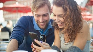Ein Mann und eine Frau schauen lachend auf ein Handy | 10 Tipps fürs perfekte Online-Dating