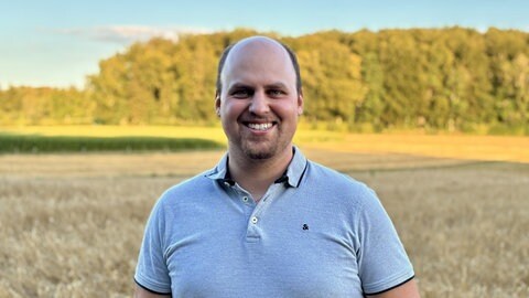 Patrick Schmelcher vom Landwirtschaftsamt Reutlingen steht vor einem Feld. Er findet es wichtig, dass neuartige Technik wie die Aussaat mit Drohnen verbreitet wird.