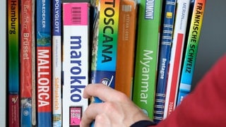 Eine Hand greift in einem Bücherregal einen Reiseführer.