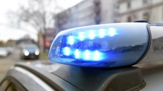 Blaulicht auf dem Dach eines Polizeiautos. Im Hintergund ist unscharf ein Wohngebiet zu erkennen.