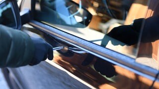 Eine Hand in einem Handschuh hält einen Schraubendreher und zekratzt damit ein Auto. In Mainz-Laubenheim hat eine unbekannte Person mindestens acht Autos beschädigt (Symbolbild)
