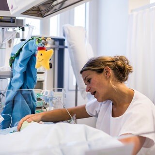 Eine Pflegefachkraft singt einem Baby etwas vor, um die Entwicklung des Frühgeborenen durch eine Musiktherapie zu unterstützen (August 2013,  Neonatologie-Intensivstation, Universitätsspital Zürich)