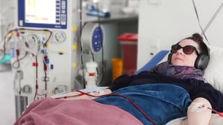 Clarissa hat MECFS und liegt in einem Krankenhausbett. Aus ihrem Arm läuft ein Schlauch für die Blutwäsche. Sie trägt eine Sonnenbrille, um Lichtreize abzuschwächen.
