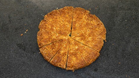 Erst Hälften, dann Viertel, dann Zwölftel: Den oberen Teil des Hefeteigs mit der karamellisierten Mandeldecke teilt SWR4 Konditor Joachim Habiger in Stücke ein, bevor er diese auf die Torte legt.