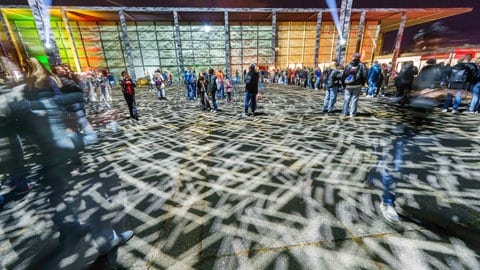 Menschen stehen auf dem Jockel-Fuchs-Platz vor der Rheingoldhalle in Mainz, der Platz ist erhellt von Lichtflecken auf dem Boden.