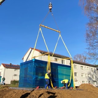 Wärmepumpe wird von einem Kran vor ein Wohnhaus positioniert
