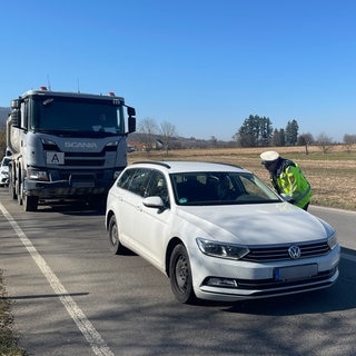 Ein Polizist steht in bei der Kontrolle in Bad Boll neben einem Auto auf der Straße und spricht mit den Insassen.