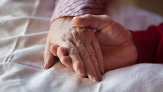 Nahaufnahme von Händen: Zwei Menschen halten sich in einem Hospiz an den Händen. In Nassau macht 2025 das erste Hospiz im Rhein-Lahn-Kreis auf.